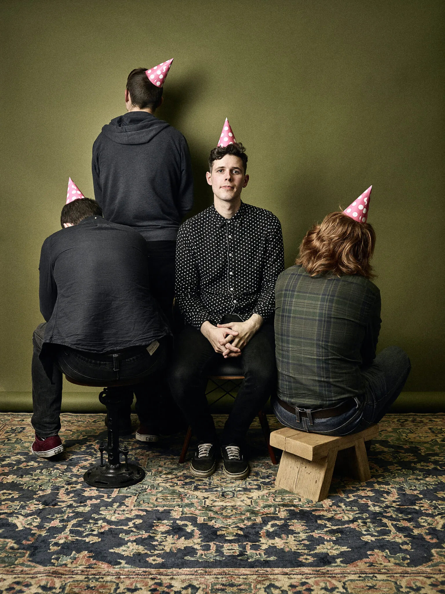 Trookers in pink party hats in front of an olive backdrop; three of the four have turned their backs to the camera